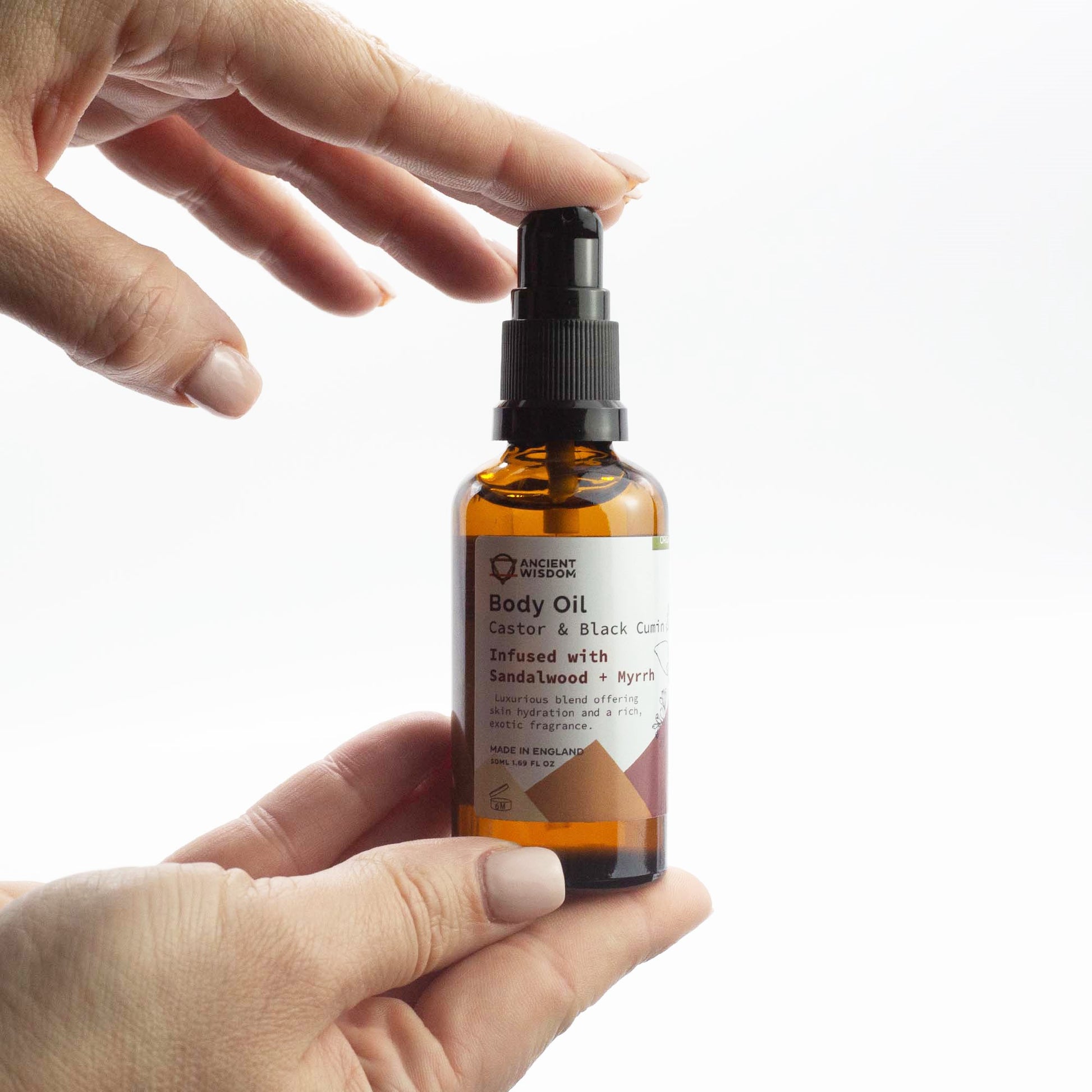 Holding a bottle of Ancient Wisdom Organic Body Oil Black Cumin & Castor Oil infused with sandalwood and myrrh