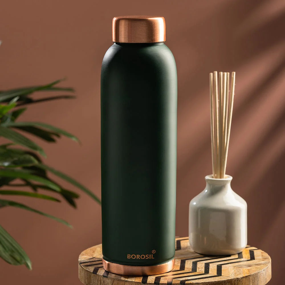 Borosil copper water bottle on a wooden table next to reed diffuser