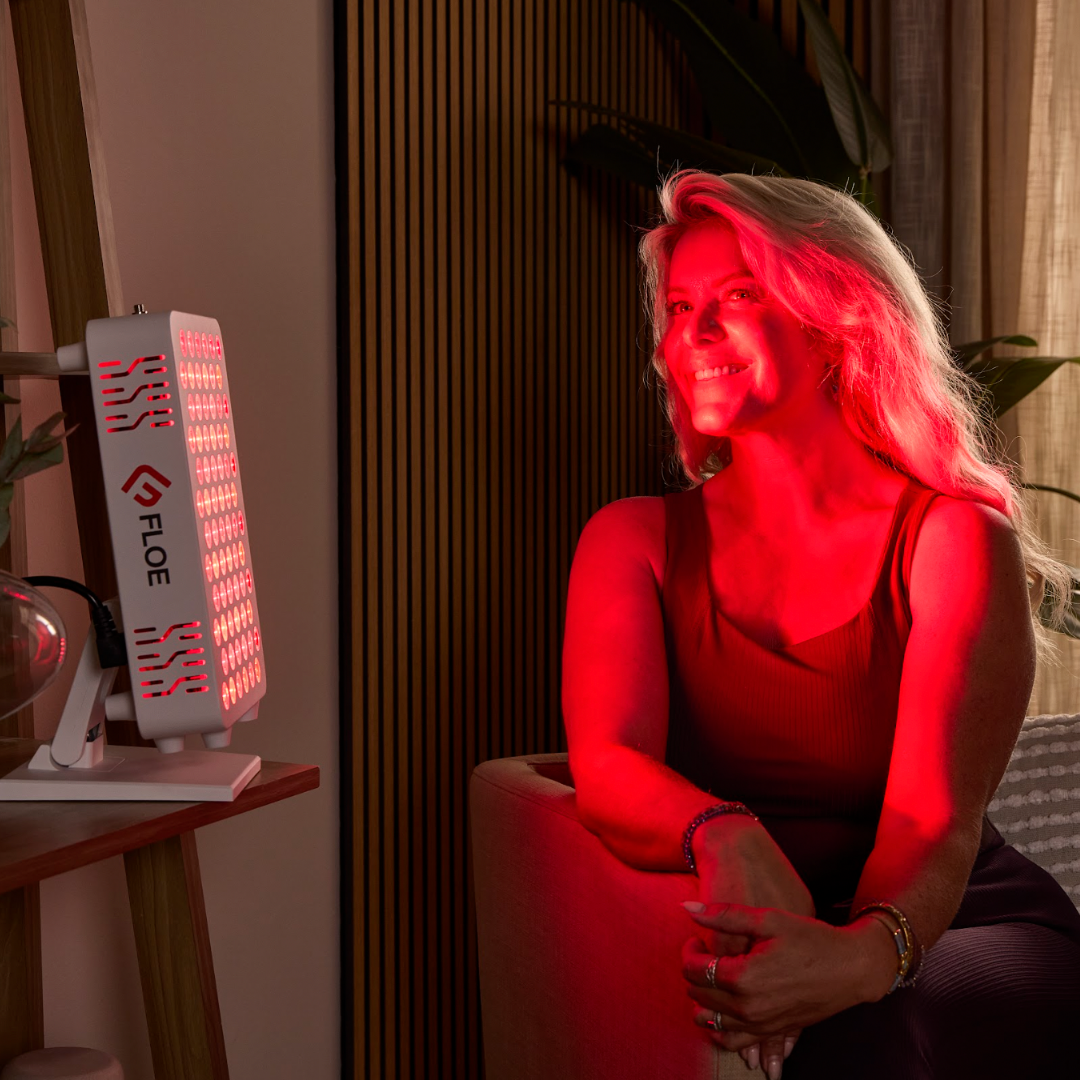 Woman sitting in a room with red light, next to a Floe red light panel.