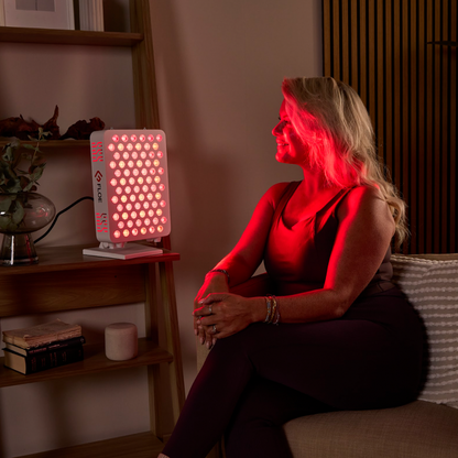 Woman receiving red light therapy with the red light panel on a shelf in a room.